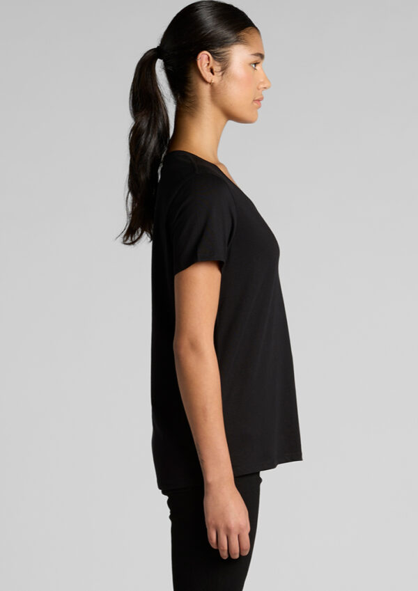 Side view of a woman wearing a loose black T-shirt and black leggings against a gray studio backdrop in a simple portrait.