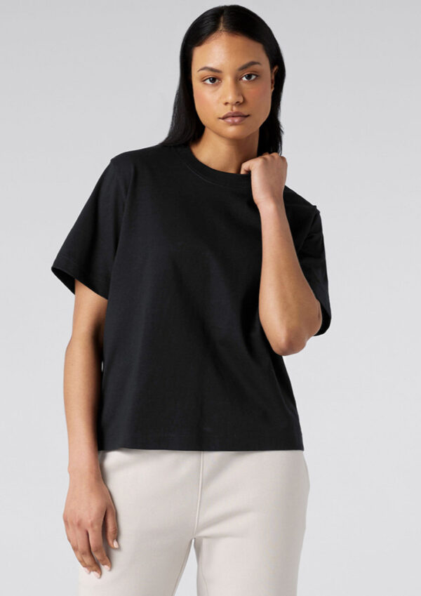 Model wearing a black short-sleeve T-shirt and light beige pants in a studio.