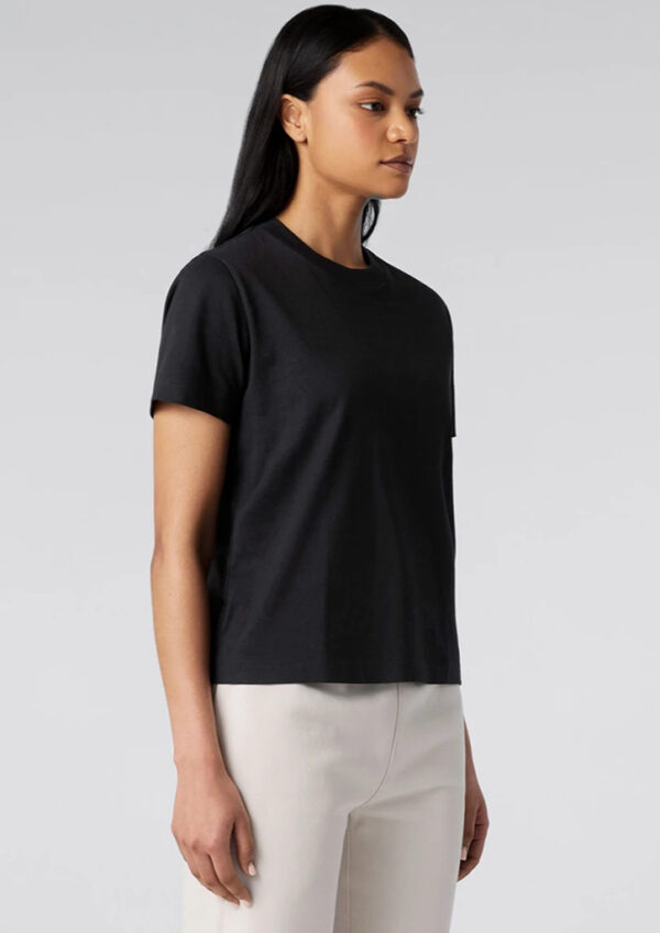 Side-profile of a person wearing a black short-sleeve T-shirt and light beige pants against a neutral backdrop.