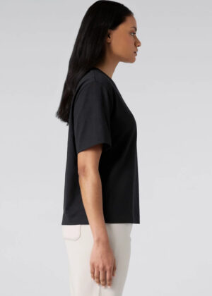 Side view of a woman wearing a black T-shirt and white pants against a light gray background.