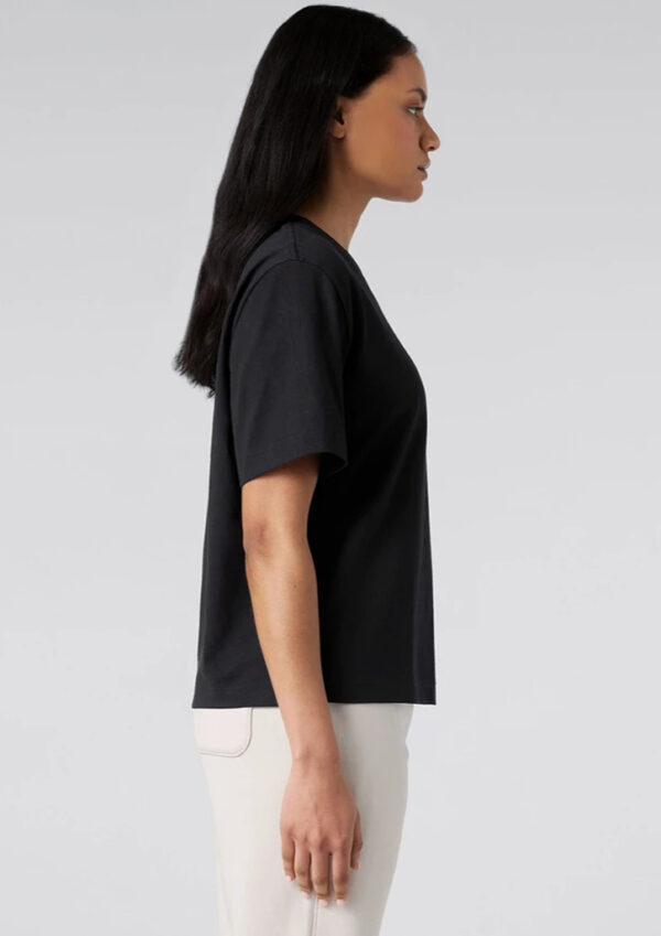 Side view of a woman wearing a black T-shirt and white pants against a light gray background.