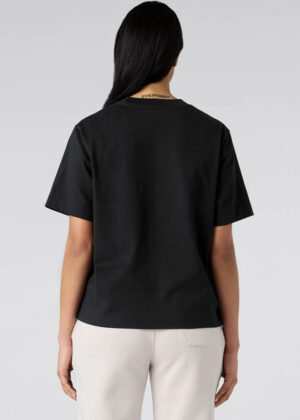 Back view of a person wearing a black short-sleeve T-shirt and light beige pants; long dark hair partially covers the neck.