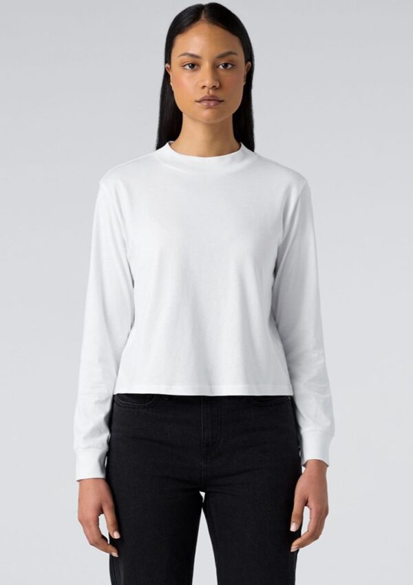 Model wearing a plain white long-sleeve crew-neck top with black jeans, standing against a light gray background.