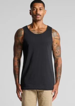 Male model wearing a black sleeveless tank top on a gray background, showcasing a fitted casual shirt with tattoos on his arms.