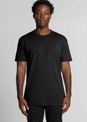 Man standing against a light gray background wearing a plain black short-sleeve T-shirt and black pants.
