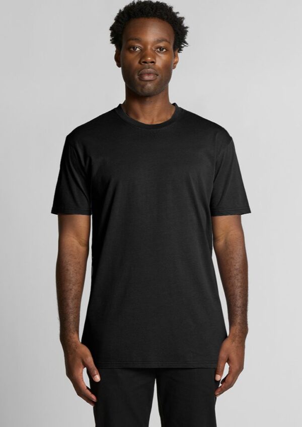 Man standing against a light gray background wearing a plain black short-sleeve T-shirt and black pants.