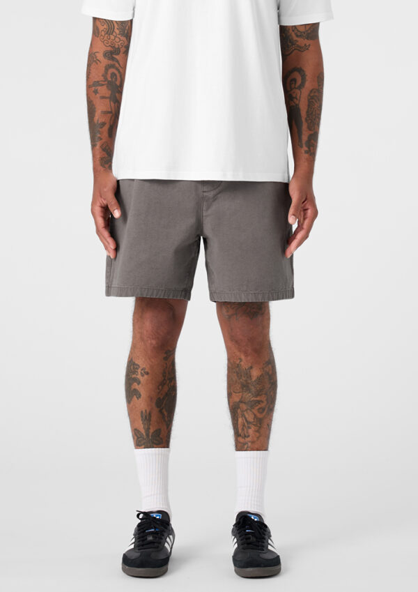 Man wearing a white T-shirt, gray shorts, white crew socks, and black sneakers, with tattoos on both arms and legs.