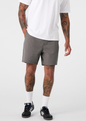 Person standing in a white T-shirt, gray shorts, white crew socks, and black sneakers with white stripes; tattoos visible on arms and legs.