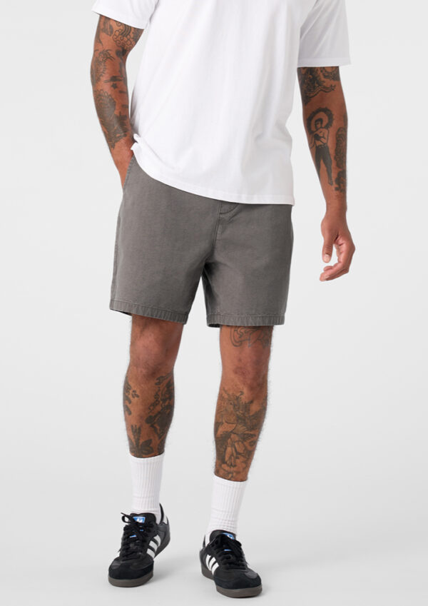 Person standing in a white T-shirt, gray shorts, white crew socks, and black sneakers with white stripes; tattoos visible on arms and legs.