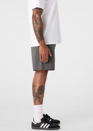 Side view of a tattooed man wearing a white T-shirt, gray shorts, white socks, and black sneakers with white stripes.