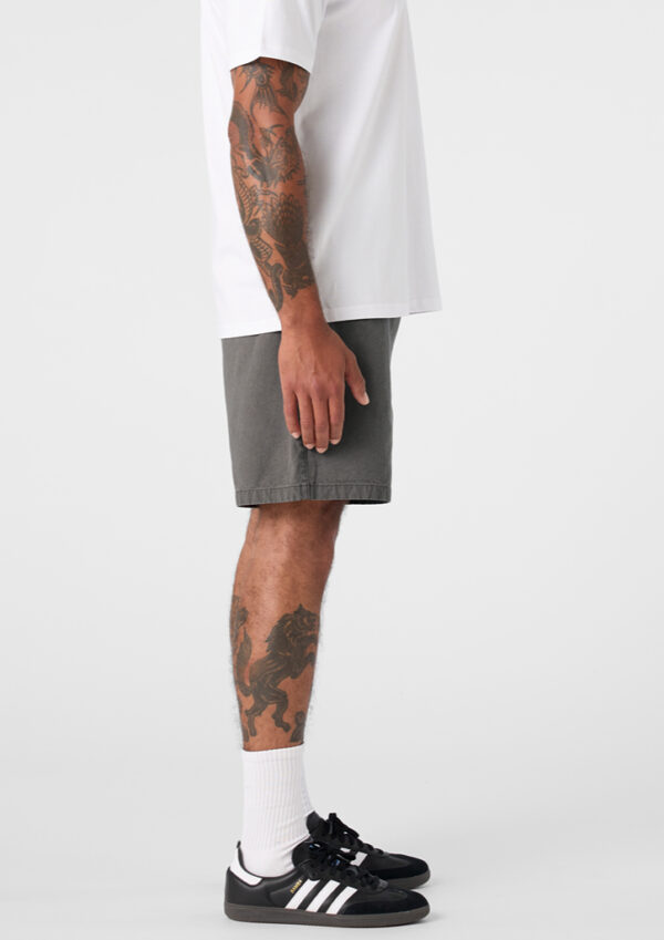 Side view of a tattooed man wearing a white T-shirt, gray shorts, white socks, and black sneakers with white stripes.