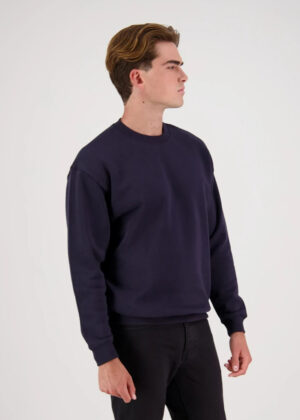 Man in a navy crewneck sweatshirt, standing in profile to the right against a white background.