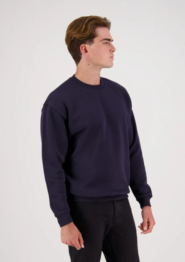 Man in a navy crewneck sweatshirt, standing in profile to the right against a white background.