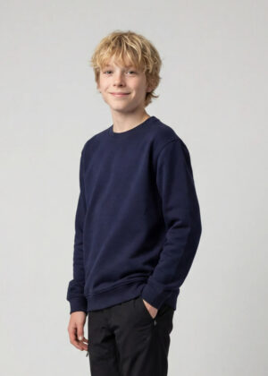 Young boy with blond hair in a navy sweatshirt and black pants, smiling at the camera against a light gray backdrop.