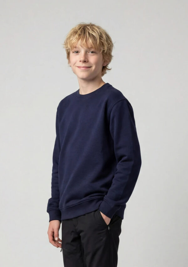 Young boy with blond hair in a navy sweatshirt and black pants, smiling at the camera against a light gray backdrop.