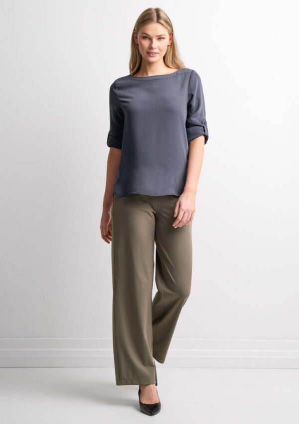 Woman wearing a blue-gray satin blouse with rolled sleeves and wide-leg taupe pants, standing against a white backdrop.