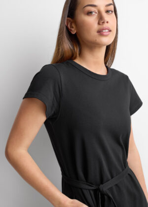Woman wearing a black short-sleeve T-shirt with a waist tie, standing against a light background.