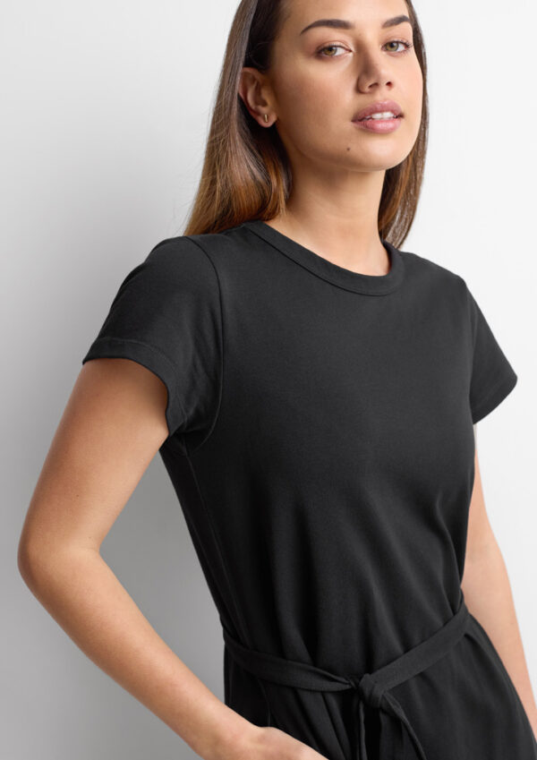 Woman wearing a black short-sleeve T-shirt with a waist tie, standing against a light background.