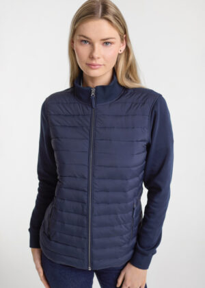 Woman wearing a navy blue quilted zip-up jacket, posing in a studio light background.