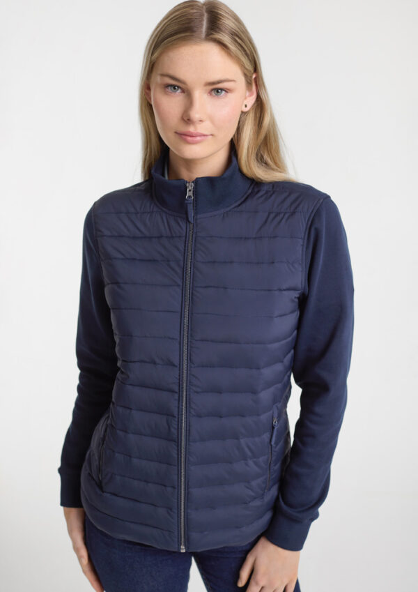 Woman wearing a navy blue quilted zip-up jacket, posing in a studio light background.