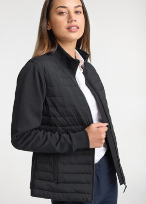 Woman modeling a black quilted zip-up jacket over a white shirt, standing against a light background.