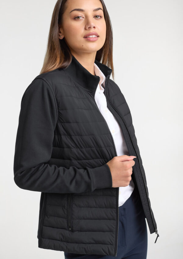 Woman modeling a black quilted zip-up jacket over a white shirt, standing against a light background.