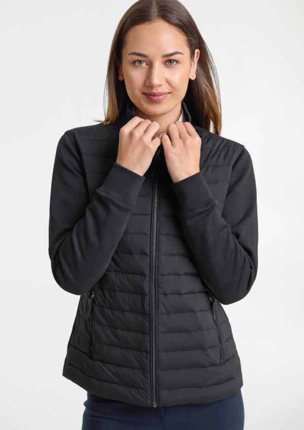 Woman wearing a black quilted zip-up vest, standing against a light background, hands near the collar as she adjusts it.