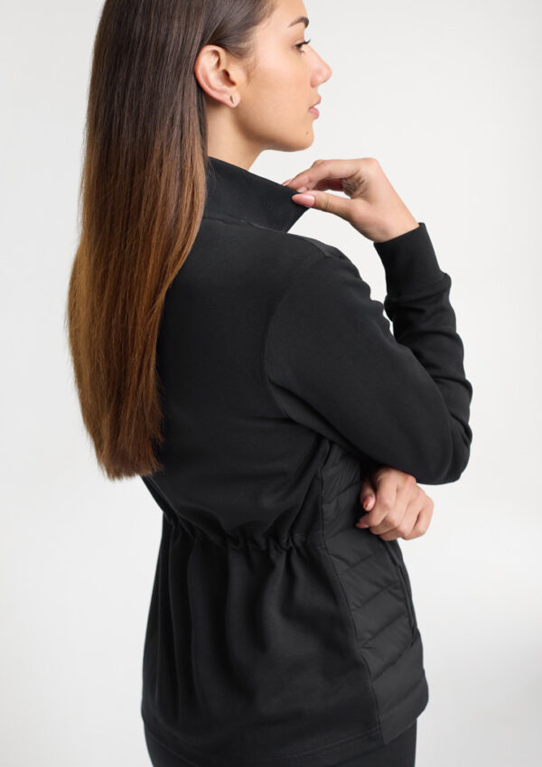 Rear view of a woman in a black jacket adjusting the collar with her right hand.