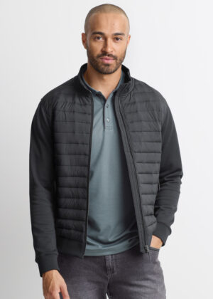 Man wearing a black quilted zip-up jacket over a teal polo, standing against a light background.