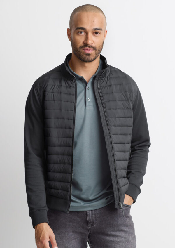 Man wearing a black quilted zip-up jacket over a teal polo, standing against a light background.