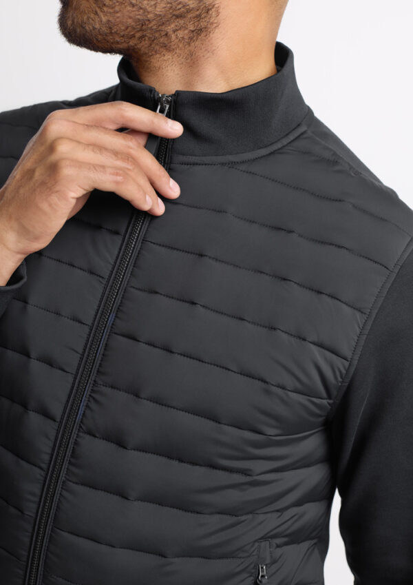 Man wearing a black quilted vest, zipping up the front zipper at the chest level.