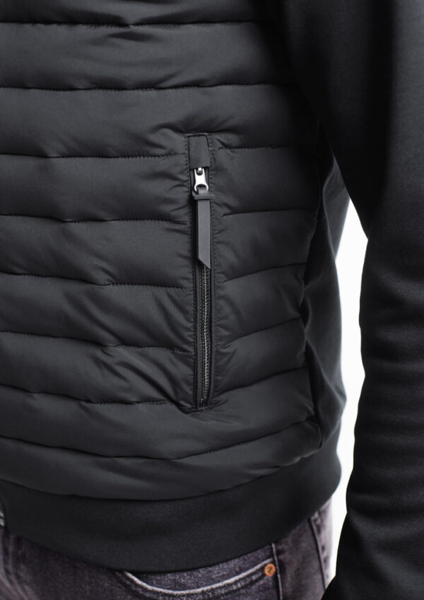 Close-up of a black puffer jacket with a vertical zippered pocket on the side, showing the zipper pull and stitching detail