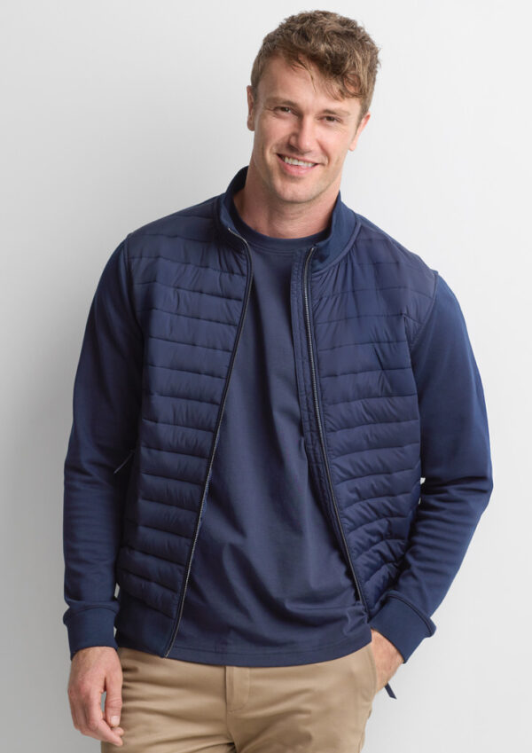 Man smiling in a navy quilted vest over a matching navy long-sleeve shirt and beige khaki pants.