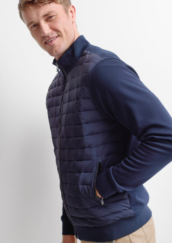 Man wearing a navy quilted vest over a navy long-sleeve shirt, standing sideways and smiling.