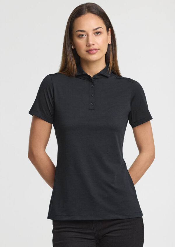 Model wearing a dark gray polo shirt with buttons, standing against a light background, hands behind her back.