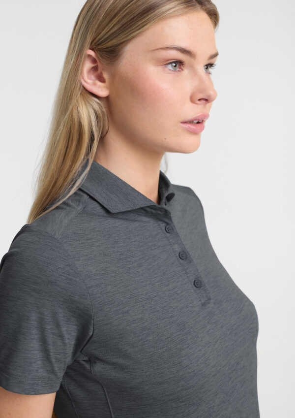 Profile of a woman with blonde hair wearing a gray polo shirt, looking to the right against a light background.