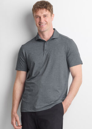 Smiling man standing against a white wall, wearing a gray polo shirt and dark pants for a casual portrait.