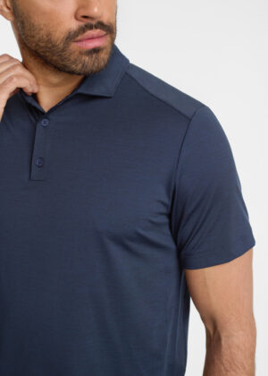 Man wearing a navy polo shirt, close-up of upper torso and face turned slightly to the left.