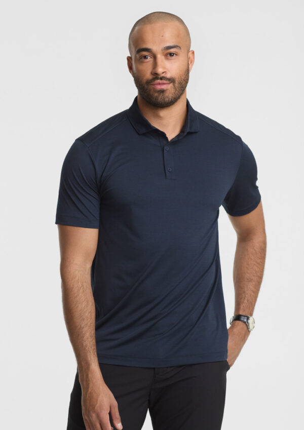 Man wearing a navy polo shirt and black pants, facing the camera with hands at his sides.