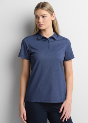 Woman wearing a blue polo shirt with short sleeves, standing against a light wall.