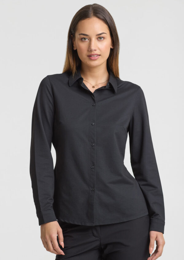 Woman in a black long-sleeve button-down shirt, standing against a pale background.