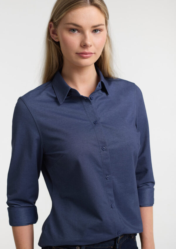 Woman wearing a navy blue button-down shirt with rolled sleeves, facing the camera against a light background.
