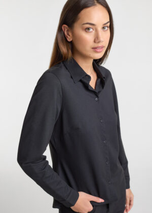 Woman in a black button-down shirt, standing in a neutral studio background, looking at the camera with a slight smile.
