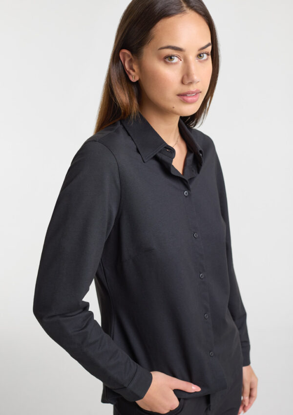Woman in a black button-down shirt, standing in a neutral studio background, looking at the camera with a slight smile.