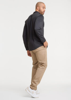 Side view of a man wearing a dark shirt with beige pants and white sneakers, hands in pockets.