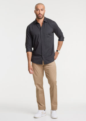 Male model wearing a black button-down shirt, tan chinos, and white sneakers, standing with one hand in his pocket.