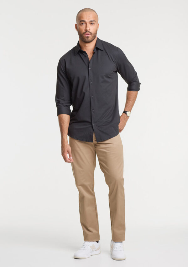 Male model wearing a black button-down shirt, tan chinos, and white sneakers, standing with one hand in his pocket.
