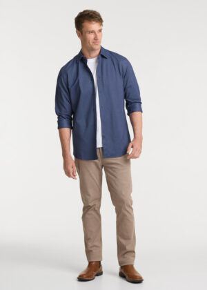Man wearing a blue button-down shirt over a white T-shirt, beige chinos, and brown Chelsea boots in a full-body pose.