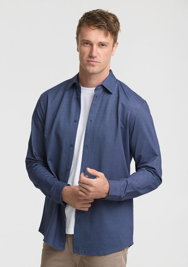 Man wearing a blue button-down shirt over a white tee, standing against a light gray background.