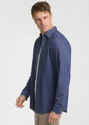 Side view of a man wearing a navy blue button-down shirt over a white T-shirt, standing against a light background.